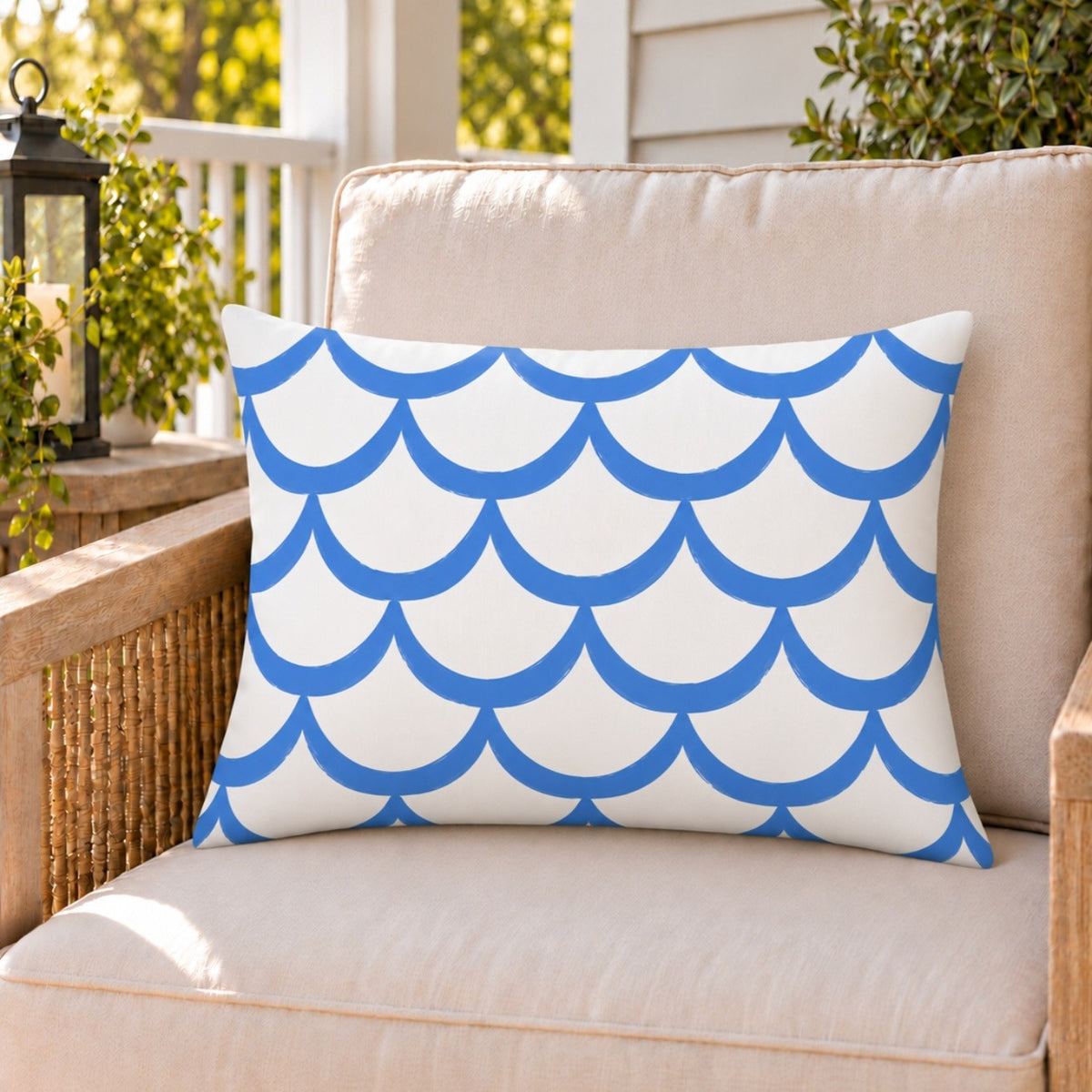 Blue painted scallop outdoor lumbar pillow on a rattan chair on a sunny summer porch