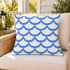 Blue painted scallop outdoor pillow on a rattan chair on a sunny summer porch