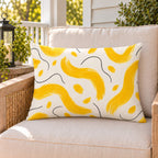 Yellow painted wave outdoor lumbar pillow on a rattan chair on a sunny summer porch
