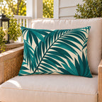 Teal palm frond outdoor lumbar pillow on a rattan chair on a sunny summer porch