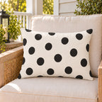 Black and white polka dot outdoor lumbar pillow on a rattan chair on a sunny summer porch