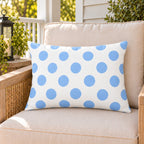 Light blue polka dot outdoor lumbar pillow on a rattan chair on a sunny summer porch
