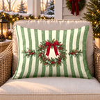 Sage stripe wreath outdoor lumbar pillow on a rattan chair on a snowy Christmas porch