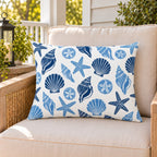 Blue seashell coastal outdoor lumbar pillow on a rattan chair on a sunny summer porch