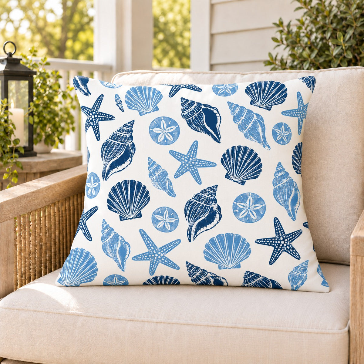 Blue seashell coastal outdoor pillow on a rattan chair on a sunny summer porch