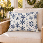 Navy snowflake outdoor lumbar pillow on a rattan porch chair with winter garland and warm lights