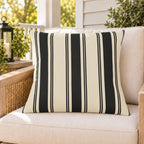 Black and cream ticking stripe outdoor pillow on a rattan chair on a sunny summer porch